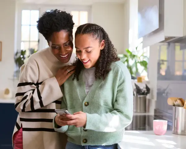 Mère et fille souriantes regardant un téléphone. Une conversation sur la pension alimentaire jusqu'à quel âge.