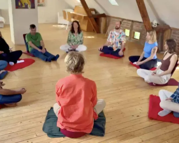 Menschen sitzen im Kreis auf Meditationskissen. Eine Gruppe genießt eine **Auszeit im Kloster**, umgeben von Ruhe und Gemeinschaft.