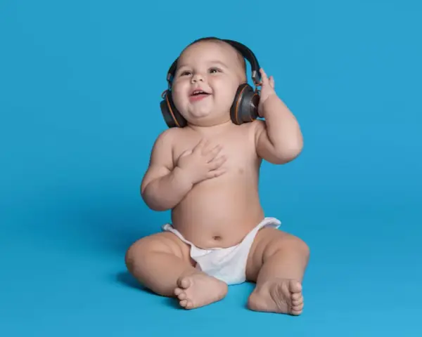 Un bébé souriant, en couche, écoute de la musique avec des écouteurs, le décibel maximum pour un bébé est à éviter.