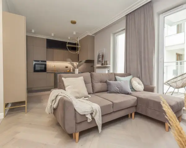 Elegancki salon z aneksem kuchennym w stylu monochromatycznym. Brązowa sofa z poduszkami, jasne drewno na podłodze.