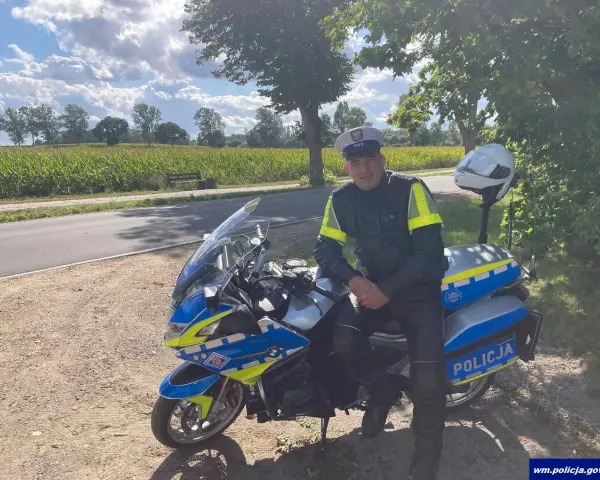 Policjant w pełnym umundurowaniu siedzi na swoim policyjnym motocyklu, gotowy do służby.