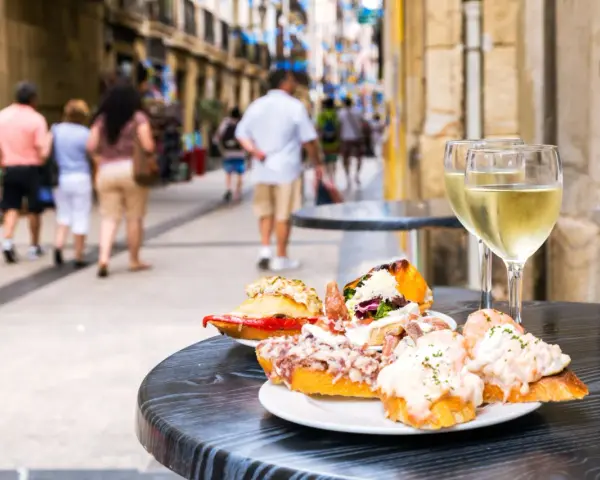 Njut av utsökt san sebastian mat och vitt vin på ett café. Folk promenerar på gatan i bakgrunden.