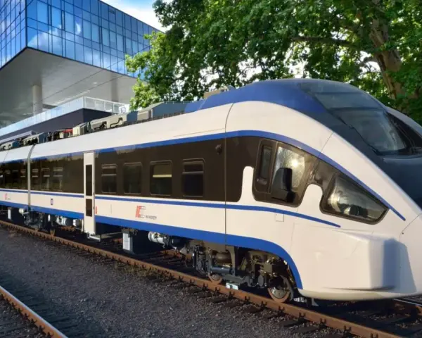 Nowoczesny, biało-niebieski pociąg Intercity ED161-002, najszybszy pociąg w Polsce, stoi na torach obok futurystycznego budynku.
