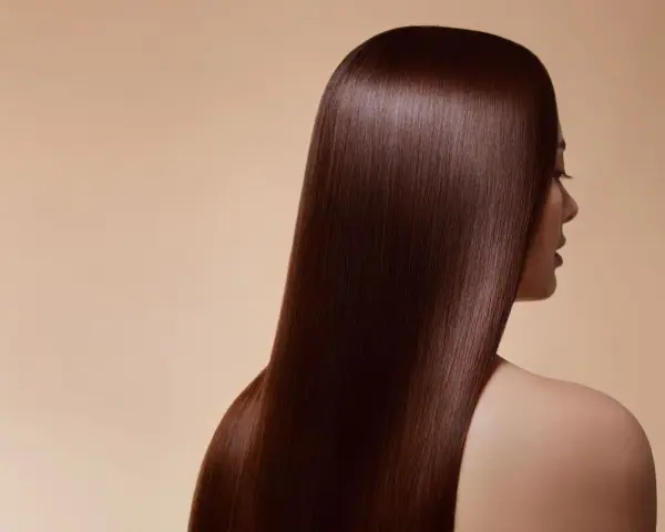 Chevelure soyeuse d'un brun profond, couleur douglas, tombant en cascade sur l'épaule d'une femme.