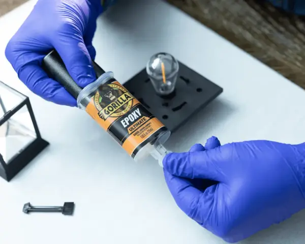 Gloves prepare to apply Gorilla Epoxy, known for its incredible strength, to a small glass and metal object.