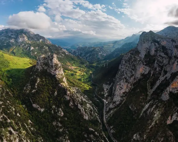 Majestätische Berge der Picos de Europa, grüne Täler und eine Straße, die sich durch die zerklüftete Landschaft schlängelt.