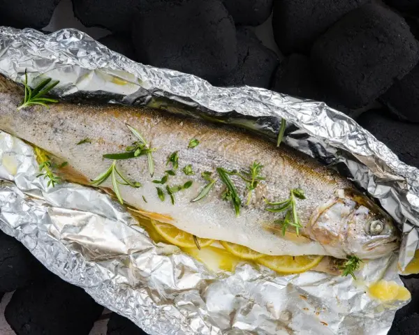 Eine ganze Forelle vom Grill in Alufolie, mit Zitronenscheiben und Rosmarin verfeinert, bereit für den Genuss.