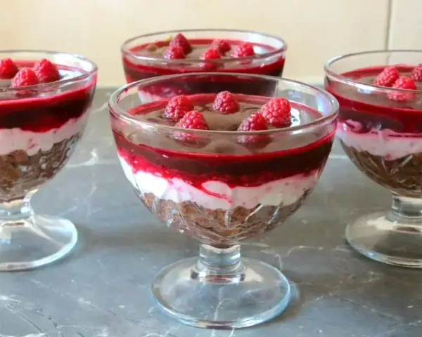 Pyszny deser z mascarpone i galaretką malinową w pucharkach, ozdobiony świeżymi malinami.