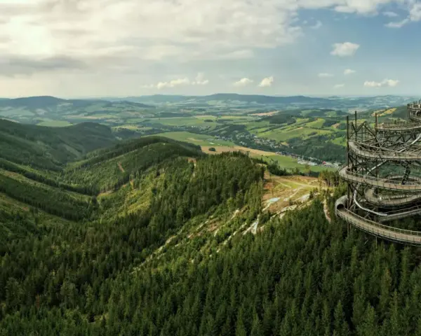 Widok na Sky Walk Czechy, spiralną wieżę widokową pośród zielonych wzgórz i lasów.