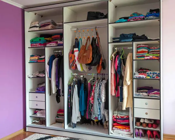 Armadio a muro con ante scorrevoli, pieno di vestiti piegati e appesi, borse e scarpe. Le dimensioni armadio camera da letto sono ben sfruttate.