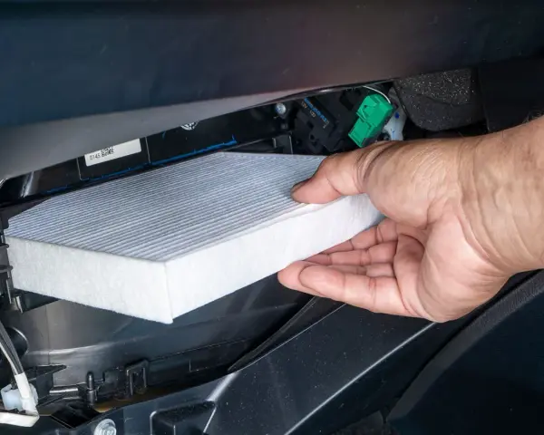 A hand removes a new cabin air filter from its packaging, ready to install it. This shows how to change cabin air filter for cleaner air.