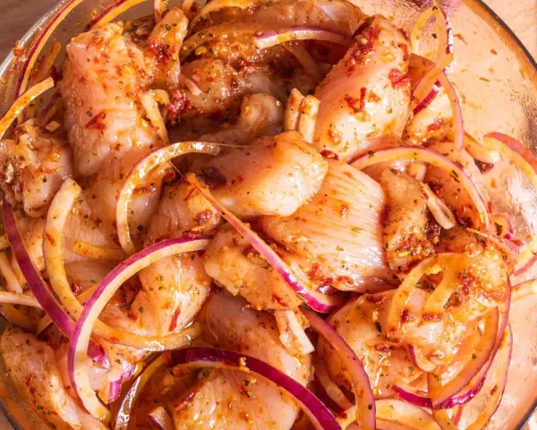Kawałki kurczaka w misce z czerwoną cebulą i przyprawami, gotowe na grill. Pyszna marynata do kurczaka na grilla.