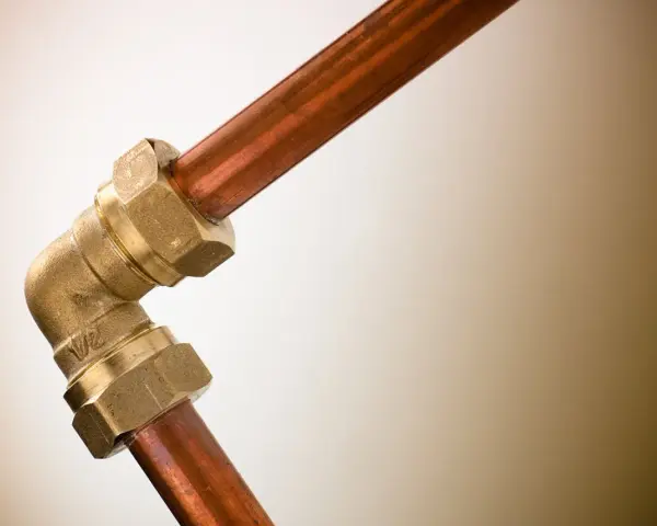 Un coude en laiton relie deux tuyaux en cuivre. Ce raccord per cuivre est essentiel pour les installations de plomberie.