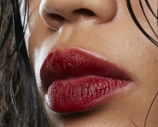 Labbra sensuali con rossetto ciliegia, un colore audace che esalta la bellezza naturale. Capelli bagnati e pelle luminosa completano il look.