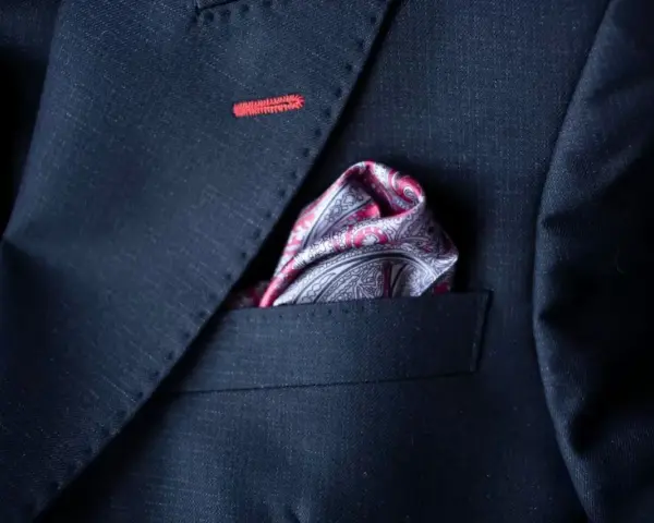 Elegancka poszetka w paisley do granatowego garnituru, z subtelnym czerwonym przeszyciem na klapie.
