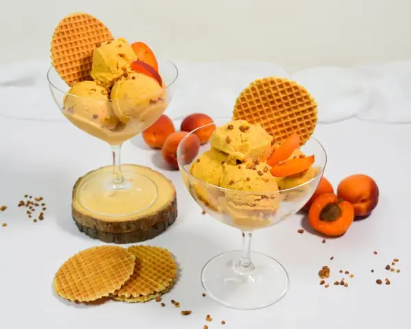 Zwei Gläser mit cremigem Aprikosen Eis, garniert mit frischen Aprikosenstücken und Waffeln. Ein sommerlicher Genuss!