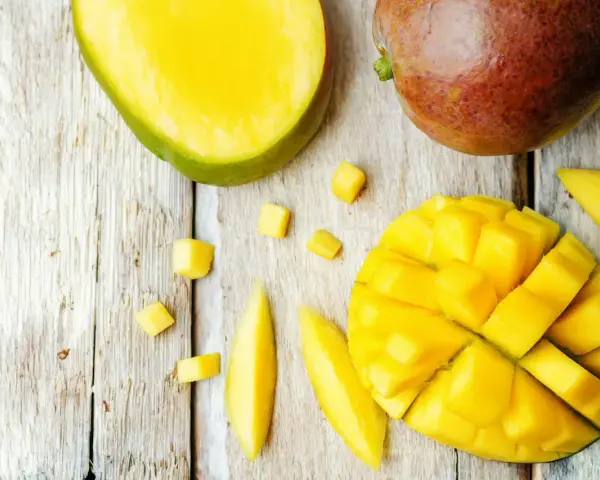 Czy pies może mango? Na drewnianym blacie leżą soczyste kawałki mango, pokrojone w kostkę i paski. Obok całe, dojrzałe owoce.