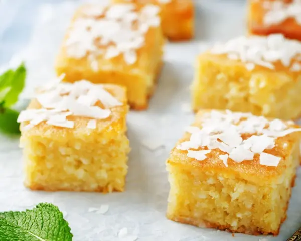 Fette di torta al cocco dorata, guarnite con scaglie di cocco e foglie di menta fresca.