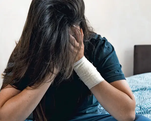 Osoba z opaską na ręce ukrywa twarz we włosach. To przykłady zachowań autodestrukcyjnych, które mogą być wołaniem o pomoc.