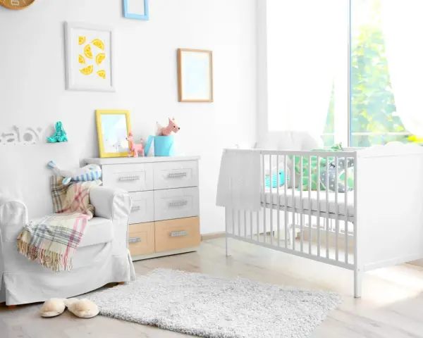 Stanza luminosa con lettino bianco, poltrona comoda e decorazioni a tema neonato. Un nido accogliente per un piccolo tesoro.