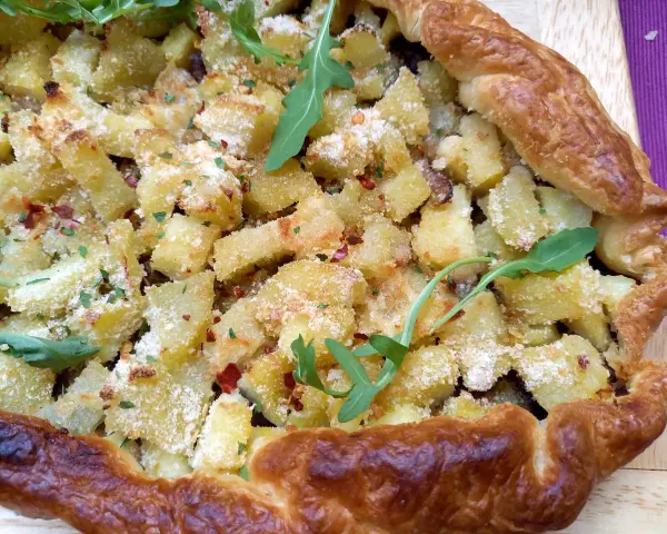 Torta salata patate e cipolle dorata e croccante, guarnita con rucola e peperoncino.