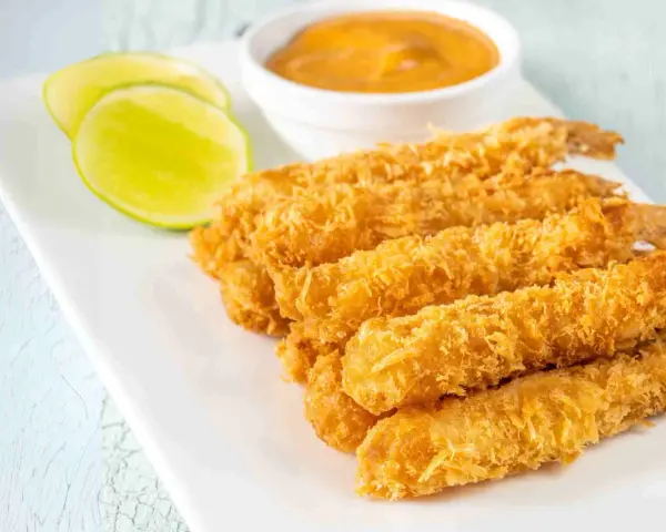 Crujientes gambas a la gabardina doradas, servidas con rodajas de lima y una salsa cremosa.