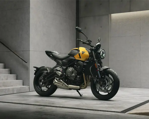 Żółty motocykl Triumph Trident 660 z czarnymi akcentami stoi na betonowej posadzce obok schodów.