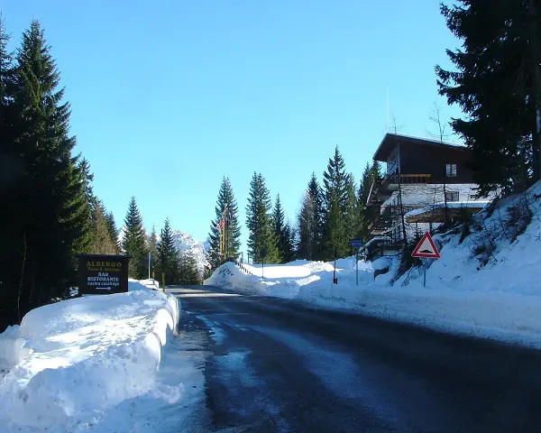 Strada innevata al passo San Antonio. Albergo e ristorante con cucina casalinga. Case di montagna e pini.
