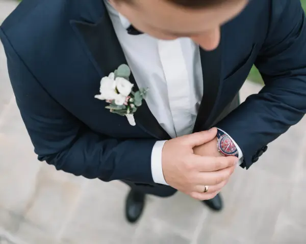 Elegancki pan młody w granatowym garniturze z butonierką co to jest, poprawia zegarek.