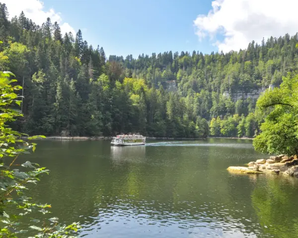 Bateau naviguant sur une rivière bordée de forêts luxuriantes, un paysage typique des chutes du Doubs.