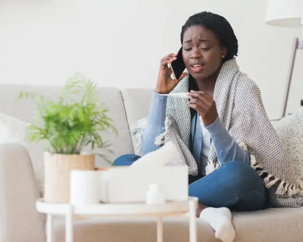 Femme malade au téléphone, thermomètre en main, elle doit se mettre en arrêt maladie avant entretien préalable licenciement.