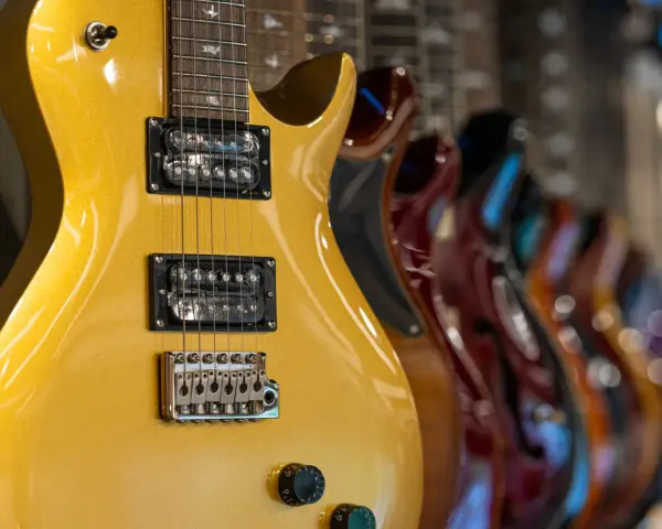 Guitarra eléctrica dorada con pastillas de **single coil** en primer plano, seguida de otras guitarras de colores.