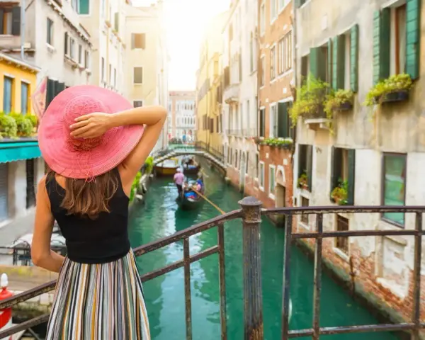 Una donna con cappello rosa ammira un canale veneziano con gondole. Un assaggio di cosa vedere a Venezia in un giorno.