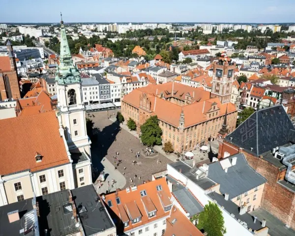 Widok na rynek i zabytkowe budynki Torunia, jednego z obiektów UNESCO w Polsce. Widać Ratusz Staromiejski i wieżę kościoła.