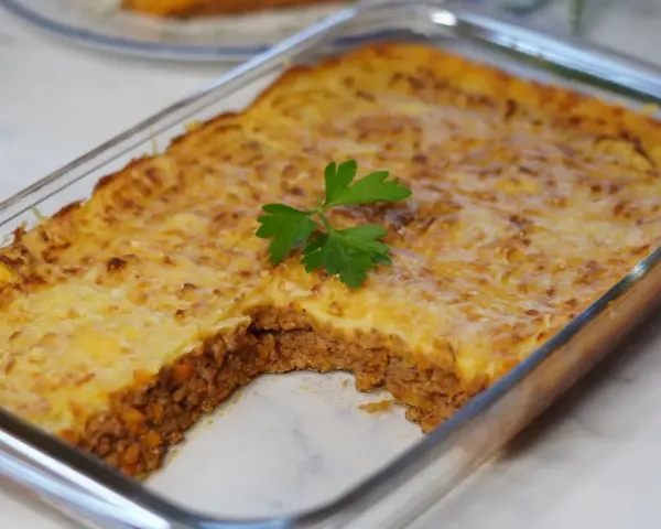 Pastel de papa recién horneado en refractario de vidrio, con una porción retirada, decorado con perejil fresco.