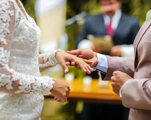 Pan młody zakłada obrączkę na palec panny młodej. W tle urzędnik udziela ślubu. Zastanawiasz się, ile kosztuje ślub cywilny?