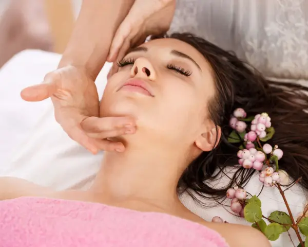 A woman receives an anti aging facial massage, her eyes closed in relaxation. Delicate pink berries adorn her dark hair.