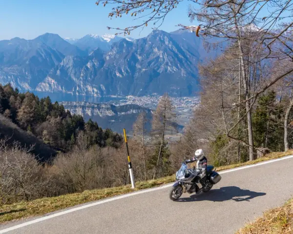 Motociclista in un panoramico motogiro Lombardia, con montagne maestose e un lago sullo sfondo.