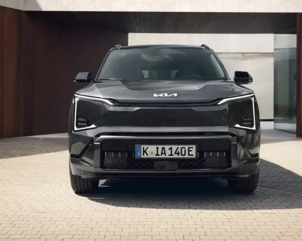 Szary SUV Kia EV5 z charakterystycznymi światłami LED, zaparkowany przed nowoczesnym budynkiem.