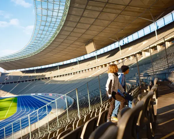 Zwei Kinder stehen auf den Rängen des Olympiastadion Berlin und blicken auf die Laufbahn.