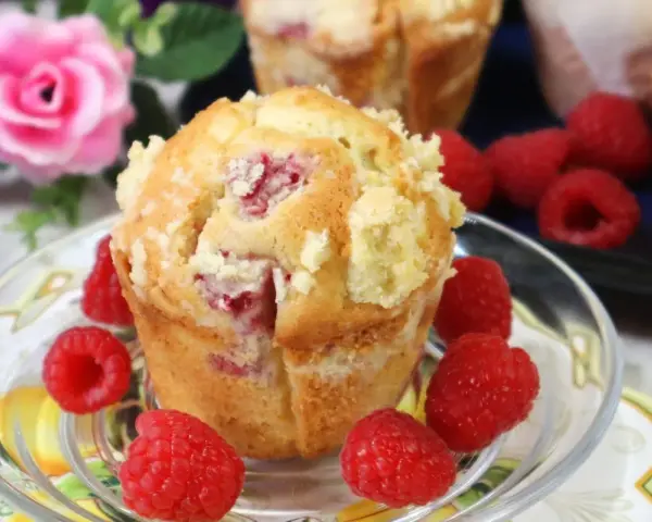 Pyszne muffinki z malinami, posypane kruszonką, otoczone świeżymi malinami.