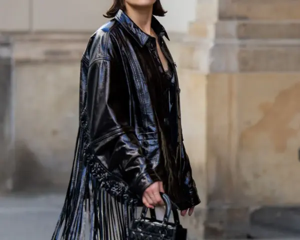 Mujer con vestido negro y chaqueta de charol con flecos. Un look audaz para combinar vestido negro con chaqueta.