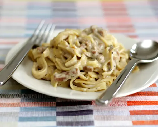 Un piatto di tagliatelle ai funghi cremose, con forchetta e cucchiaio pronti per gustare questo delizioso primo.