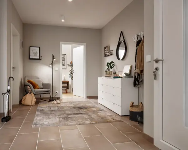 Stilvoller Flur gestalten: Grauer Sessel, Teppich, weiße Kommode mit Spiegel und Garderobe schaffen eine einladende Atmosphäre.