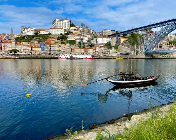 A traditional Rabelo boat with barrels, a symbol of Porto's wine heritage, floats on the Douro River. This iconic view is a must-see for any Porto travel guide.