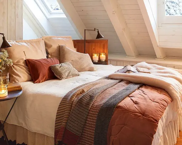 Dormitorios cálidos y acogedores bajo un techo abuhardillado. Cama con mantas de punto y cojines mullidos. Velas y flores crean un ambiente íntimo.
