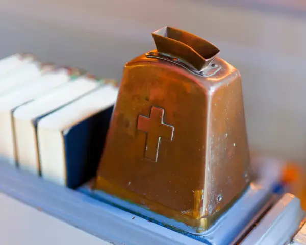 Kupferne Klingel mit Kreuz, bereit für Spenden. Hier wird über Kirchensteuer Befreiung nachgedacht.