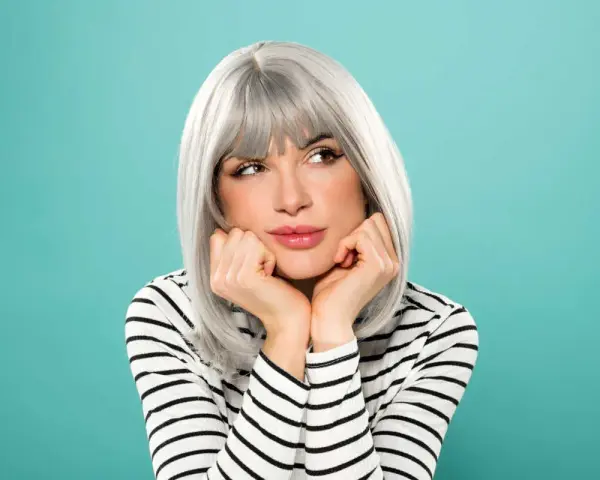 Donna con eleganti capelli grigi, appoggiata alle mani, con un'espressione sognante.