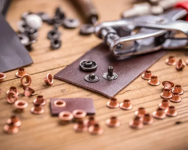 Narzędzia i nity do nitowania ręcznego skóry. Skórzane kawałki, metalowe nity i szczypce do nitowania na drewnianym blacie.