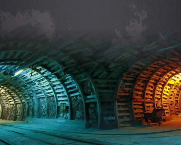 Wnętrze kopalni Nowa Ruda. Tunel oświetlony niebieskim i pomarańczowym światłem, z drewnianymi podporami i torami kolejowymi.